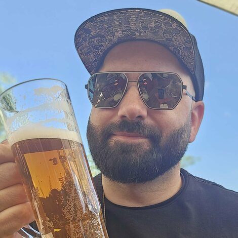 Junger Mann mit Bart, Sonnenbrille und Basecap schaut großes Bierglas an