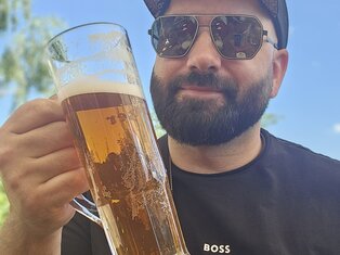 Junger Mann mit Bart, Sonnenbrille und Basecap schaut großes Bierglas an