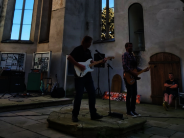 Zwei Männer spielen Gitarre in einer Kirche ohne Dach