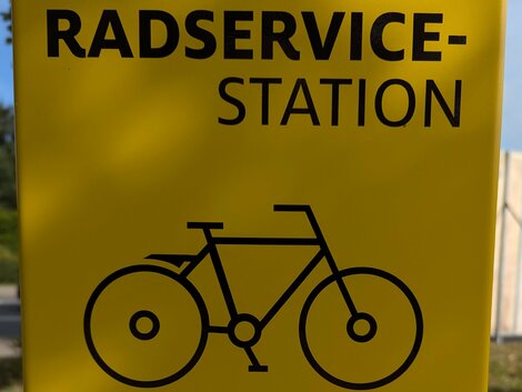 Schwarzer Aufdruck mit "Radservicestation" und einem Fahrrad- und Werkzeugpiktogamm auf gelben Grund